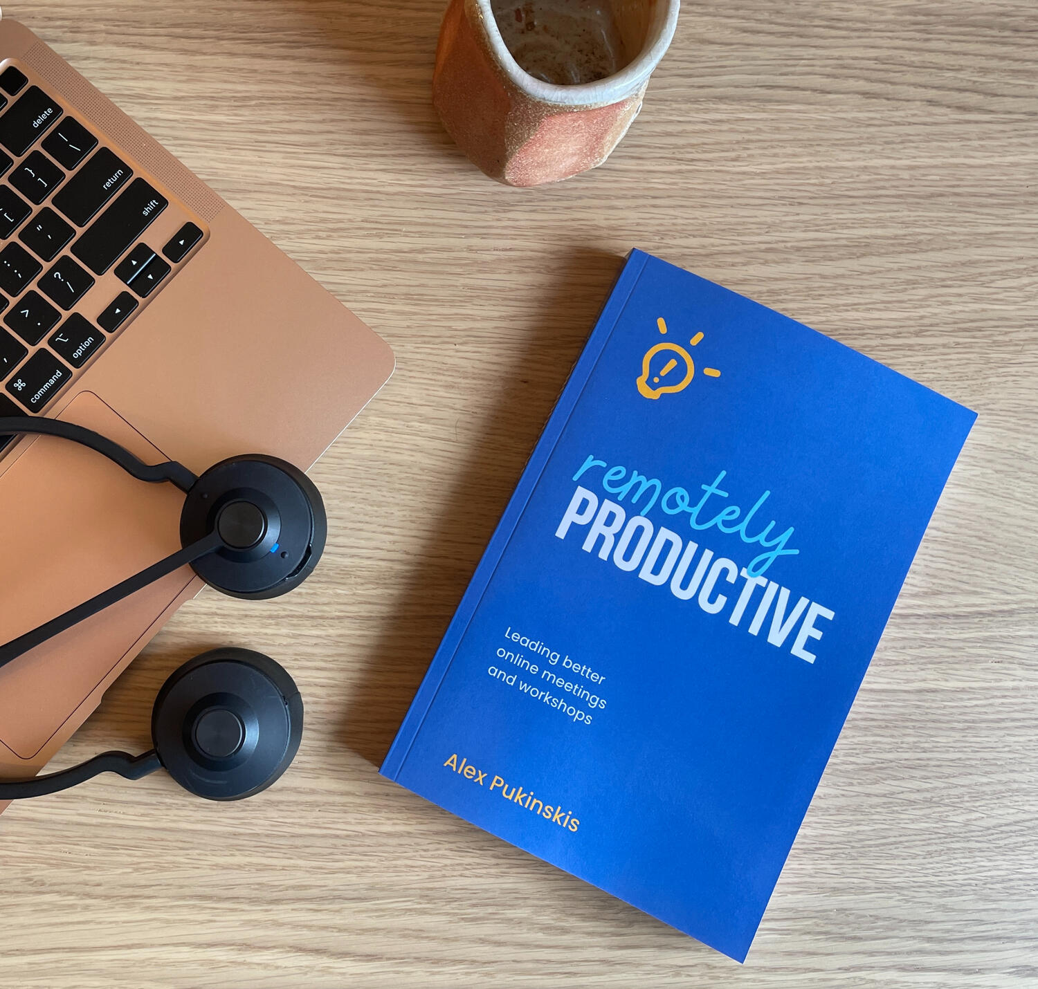 The blue cover of the book 'Remotely Productive', pictured with laptop, headset, and calming wood-fired ceramic mug